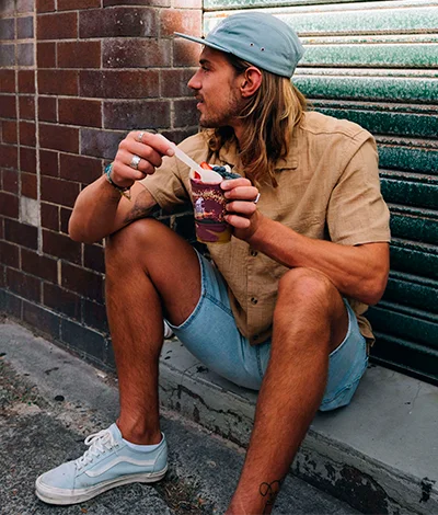 A person sitting on the ground eating an OAKBERRY Bowl